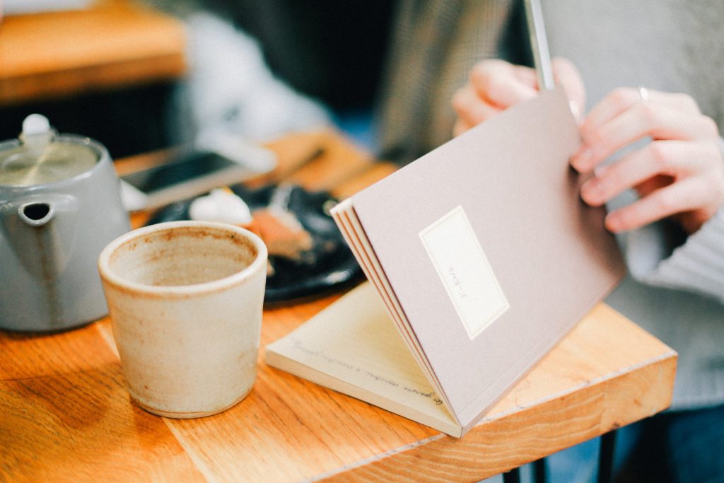 Someone sitting in front of a table with a cup of coffee, a journal and breakfast on it