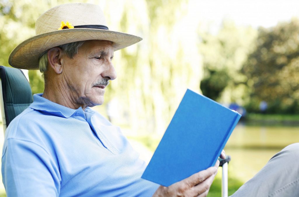 Older man sitting outside reading a book
