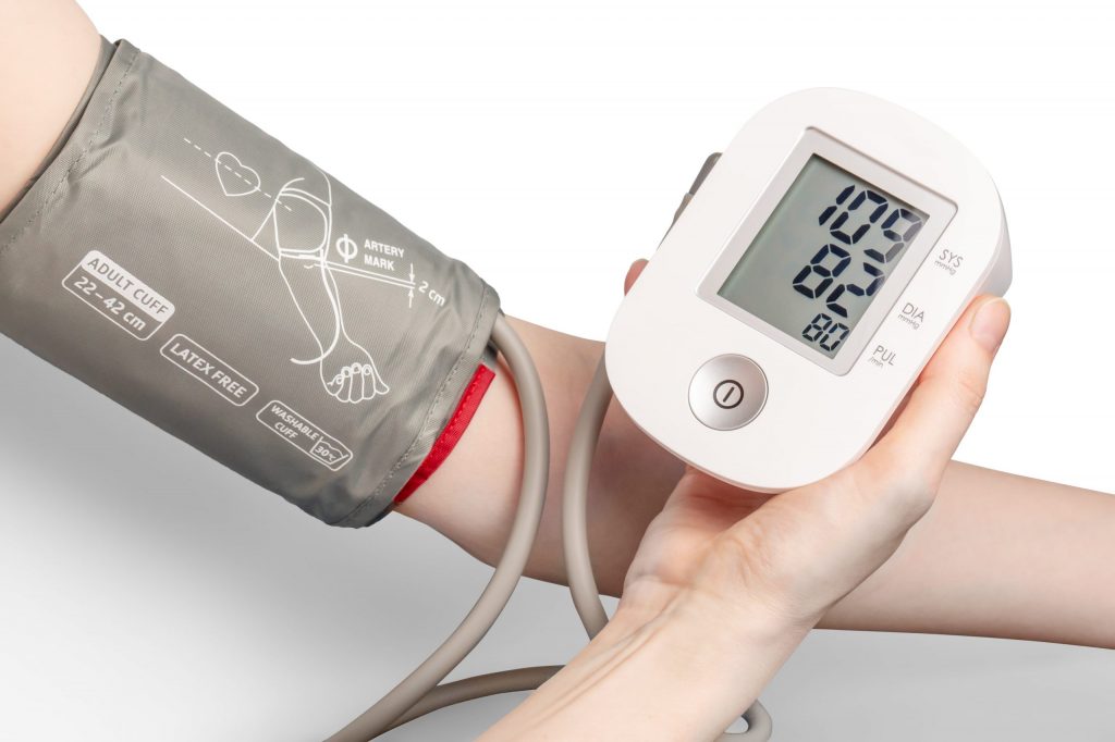 someone holding a blood pressure machine with arm wearing blood pressure cuff in the backgroud