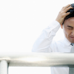 business man leaning on a railing with his hands on his head