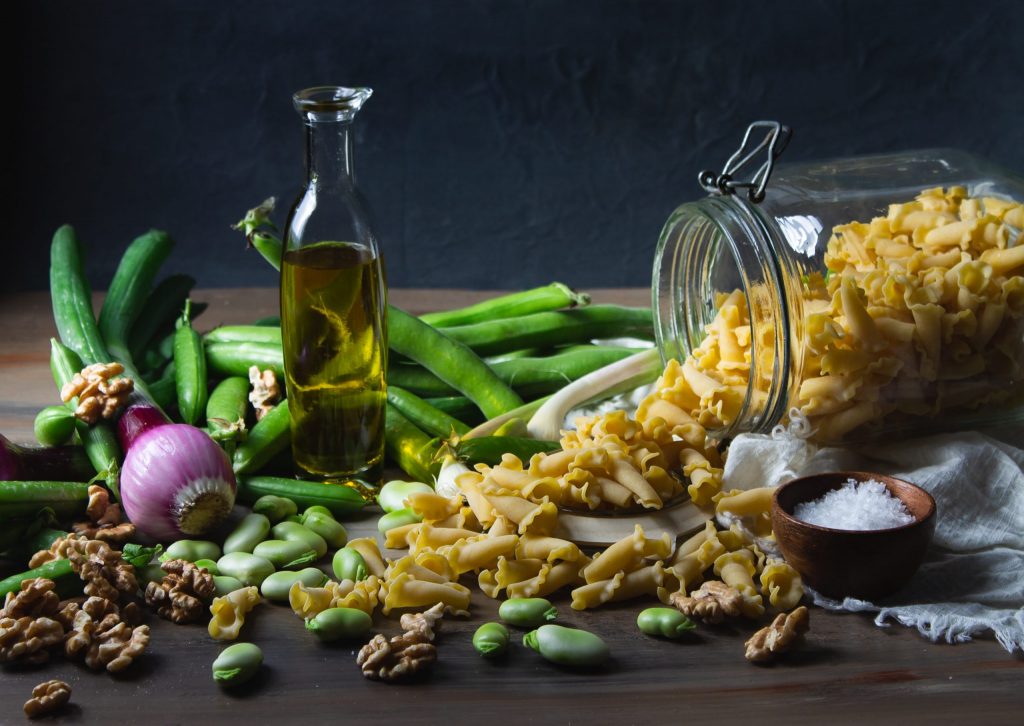 Bottle of cooking oil sitting on a table with onions and pasta