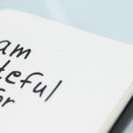 A hand writing "I am grateful for" in a journal