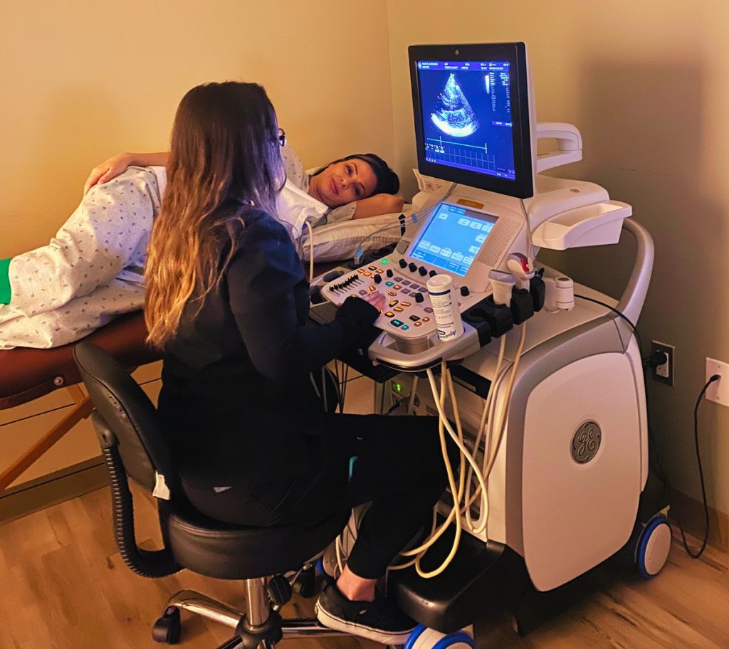 Woman sitting in a chair conducting an ultrasounds on a woman laying on a treatment bed.